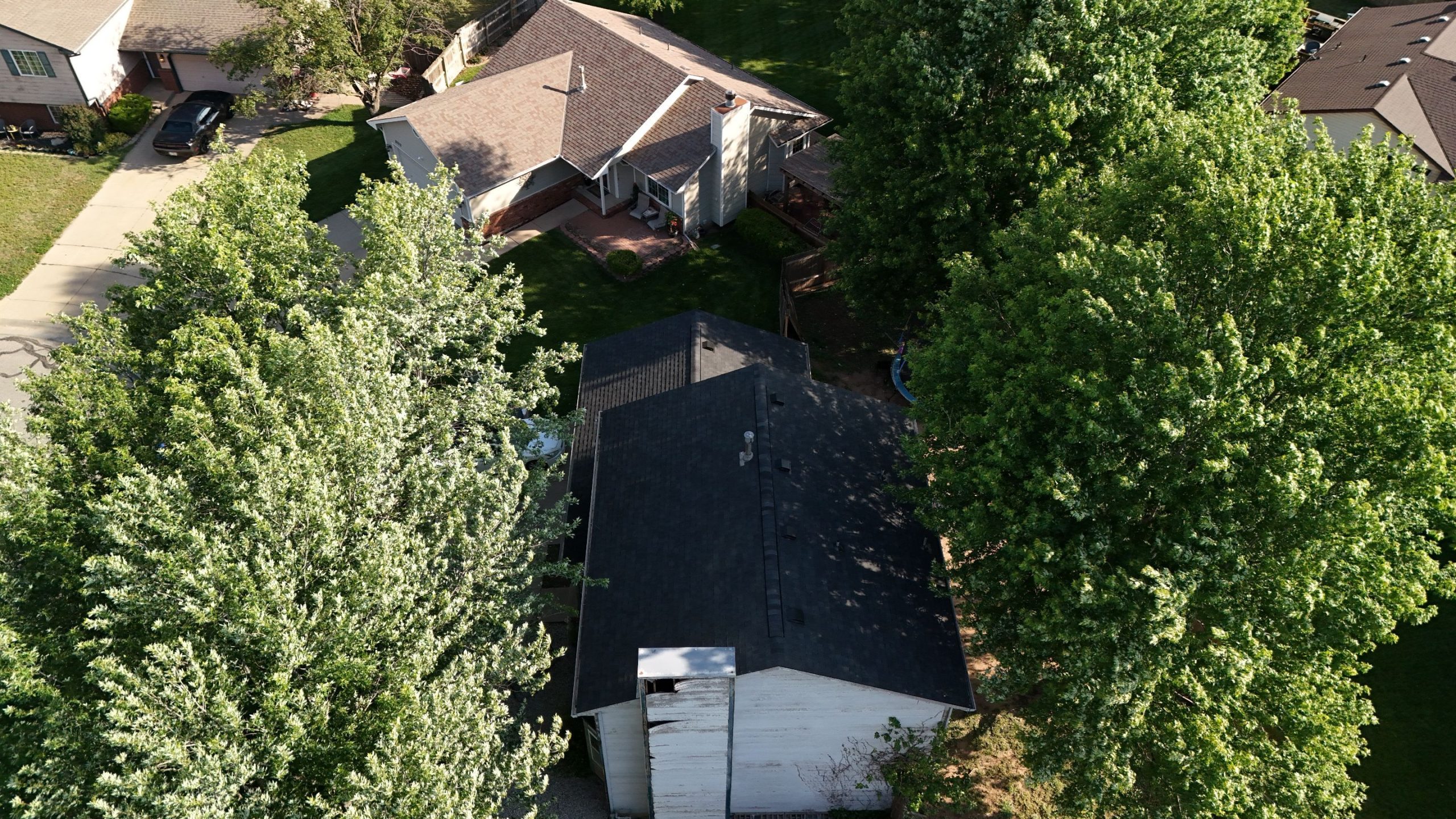default Solid Rock Commercial Roofing Aerial view of a suburban neighborhood showing a central house with a dark roof, a driveway with a car, and surrounding green lawns and large trees.