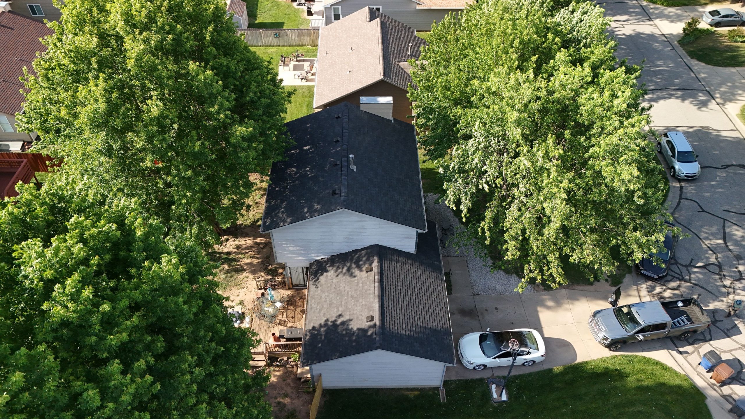 Aerial view of a suburban street with tree-lined blocks, houses with pitched roofs, and several parked cars.
