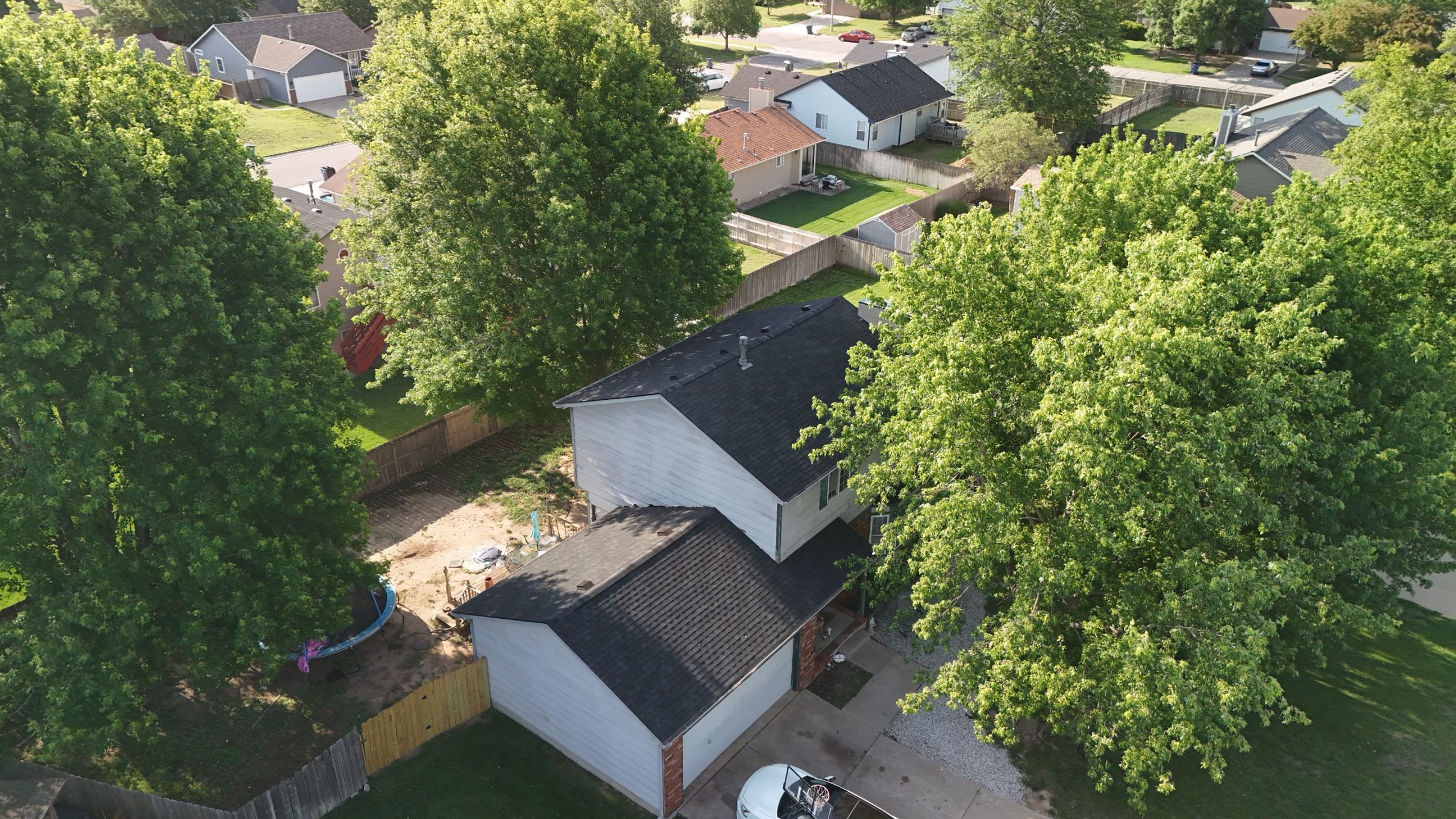 default Solid Rock Commercial Roofing Aerial view of a suburban neighborhood with tall trees, white houses, fenced yards, and a curved street nearby.