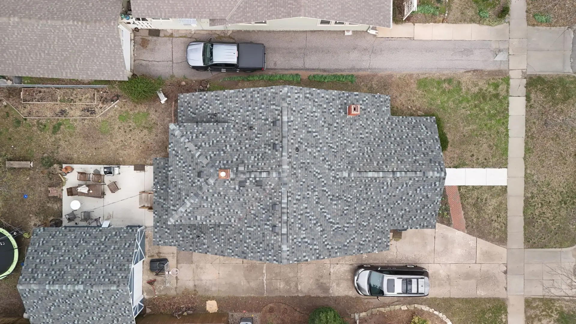 Aerial view of a suburban block: gray shingle roofs, a black pickup in a driveway, and sidewalks along the street