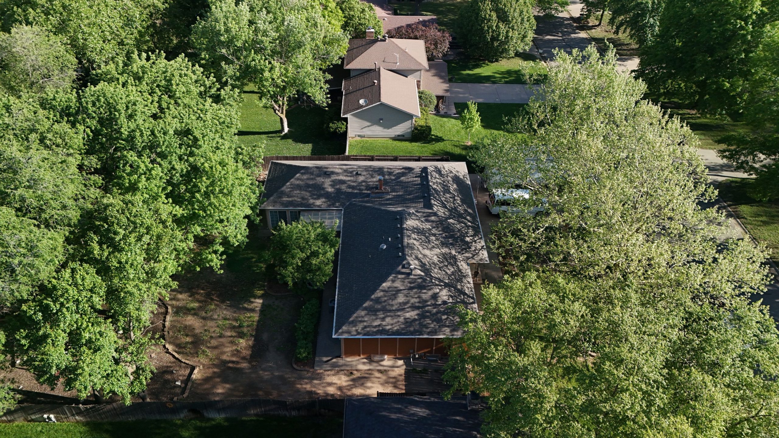 default Solid Rock Commercial Roofing Aerial view of a suburban neighborhood with roofs, lawns, and dense green trees lining the streets and yards.