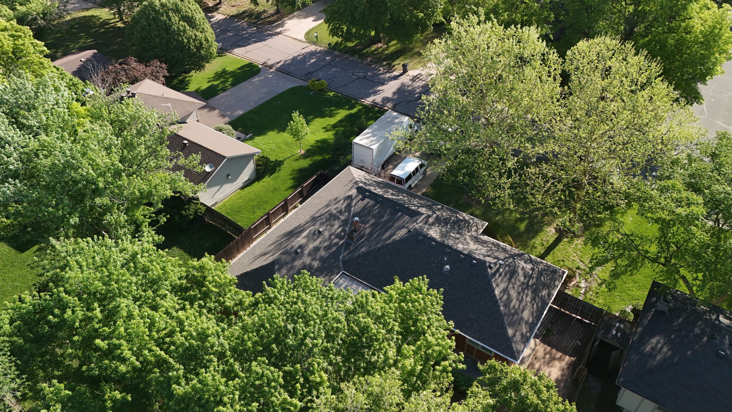 default Solid Rock Commercial Roofing Aerial view of a suburban neighborhood with green lawns, trees, and a white moving truck parked near a house.