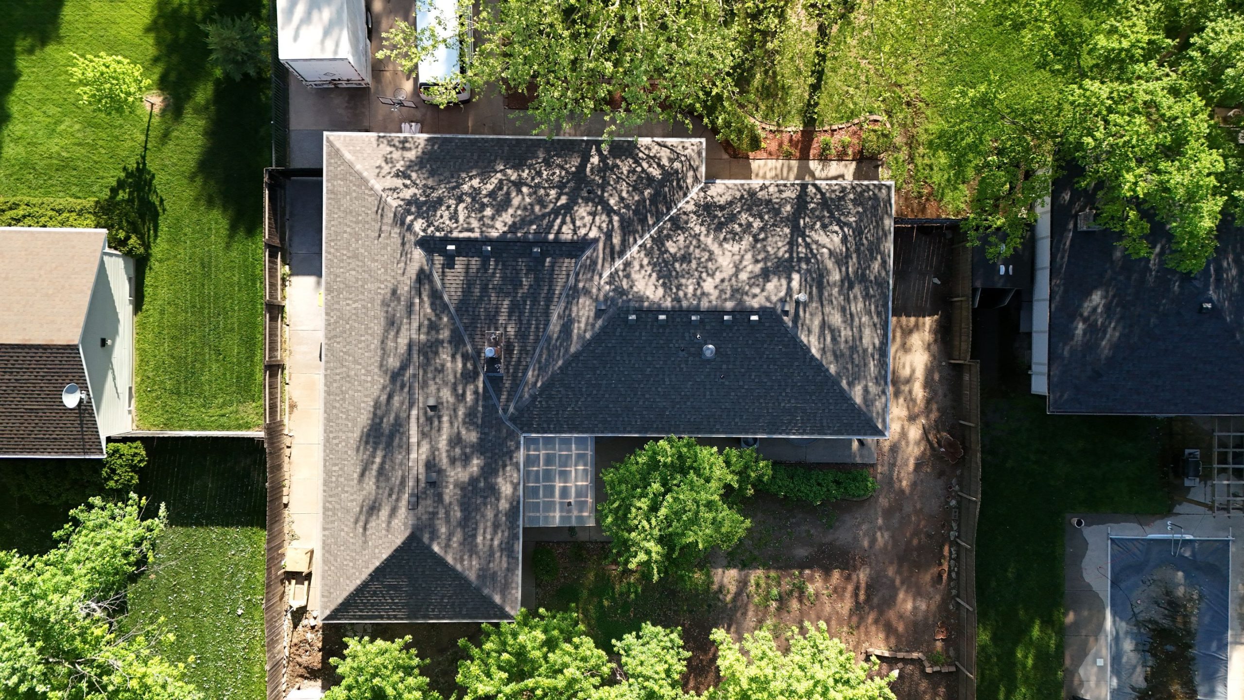 Aerial view of a gray-roofed house with surrounding green trees and a manicured backyard area.