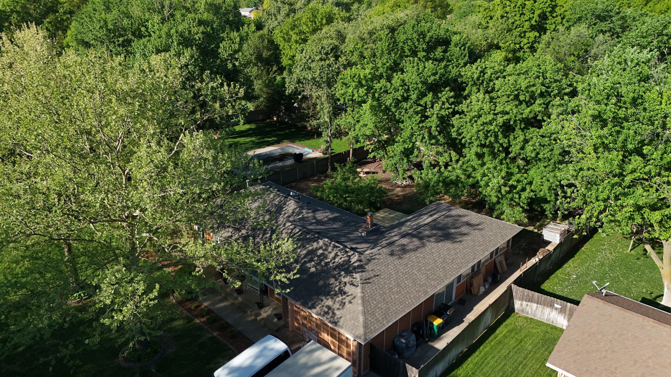 default Solid Rock Commercial Roofing Aerial view of a suburban house surrounded by dense green trees, with a fenced backyard and a small pool nearby.